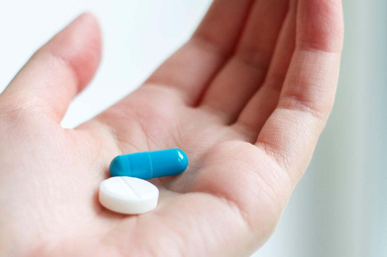 Blue and white pill capsule on the female palm on white background. Antidepressant pills in female hand. Female hand holding a pill on the palm