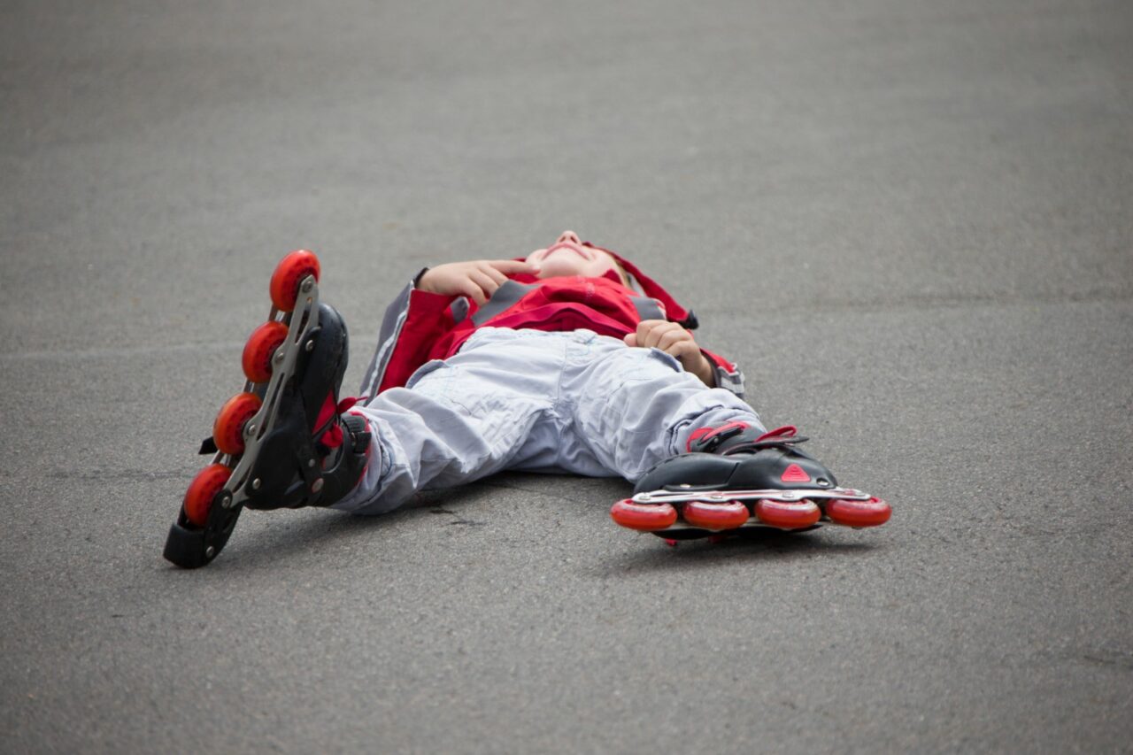 The boy in roller skates lying on the pavement.The child in roll