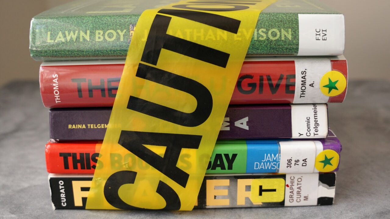 A stack of books found on frequently banned book lists wrapped in caution tape.