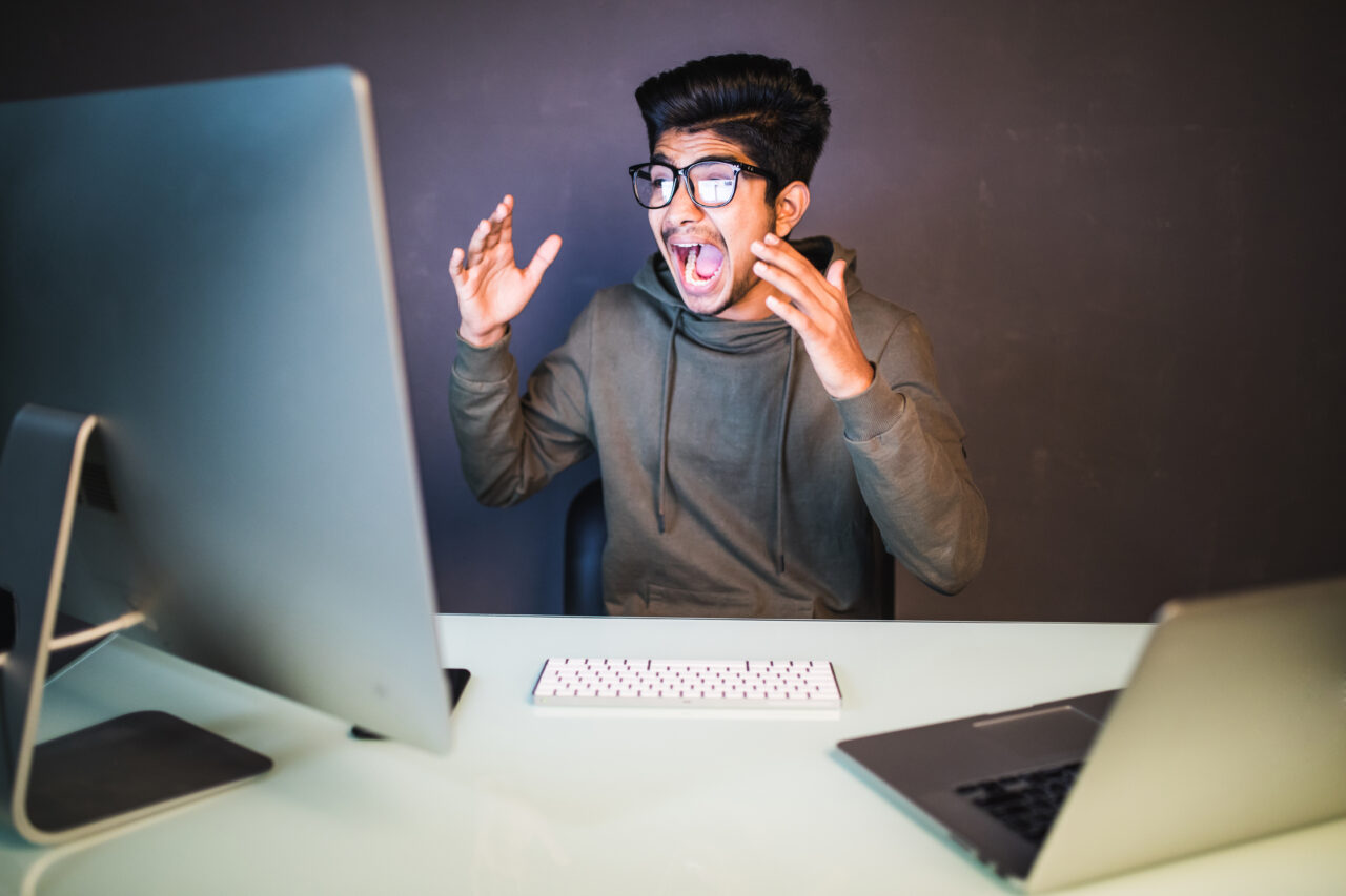 Indian angry screaming young programmer at pc computer at dark office