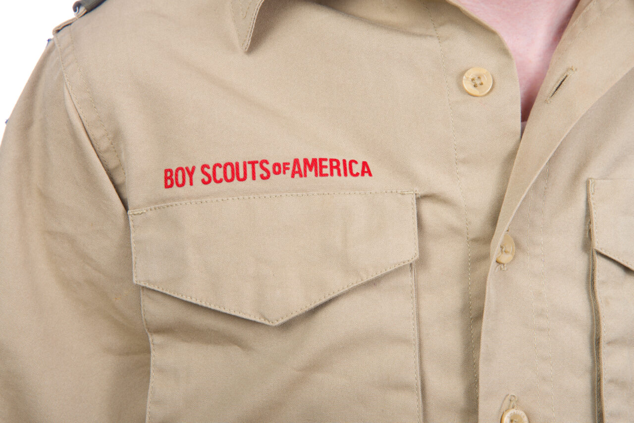 Close up on a young caucasian boy wearing tan Boy Scouts of America shirt pocket with logo above in red.
